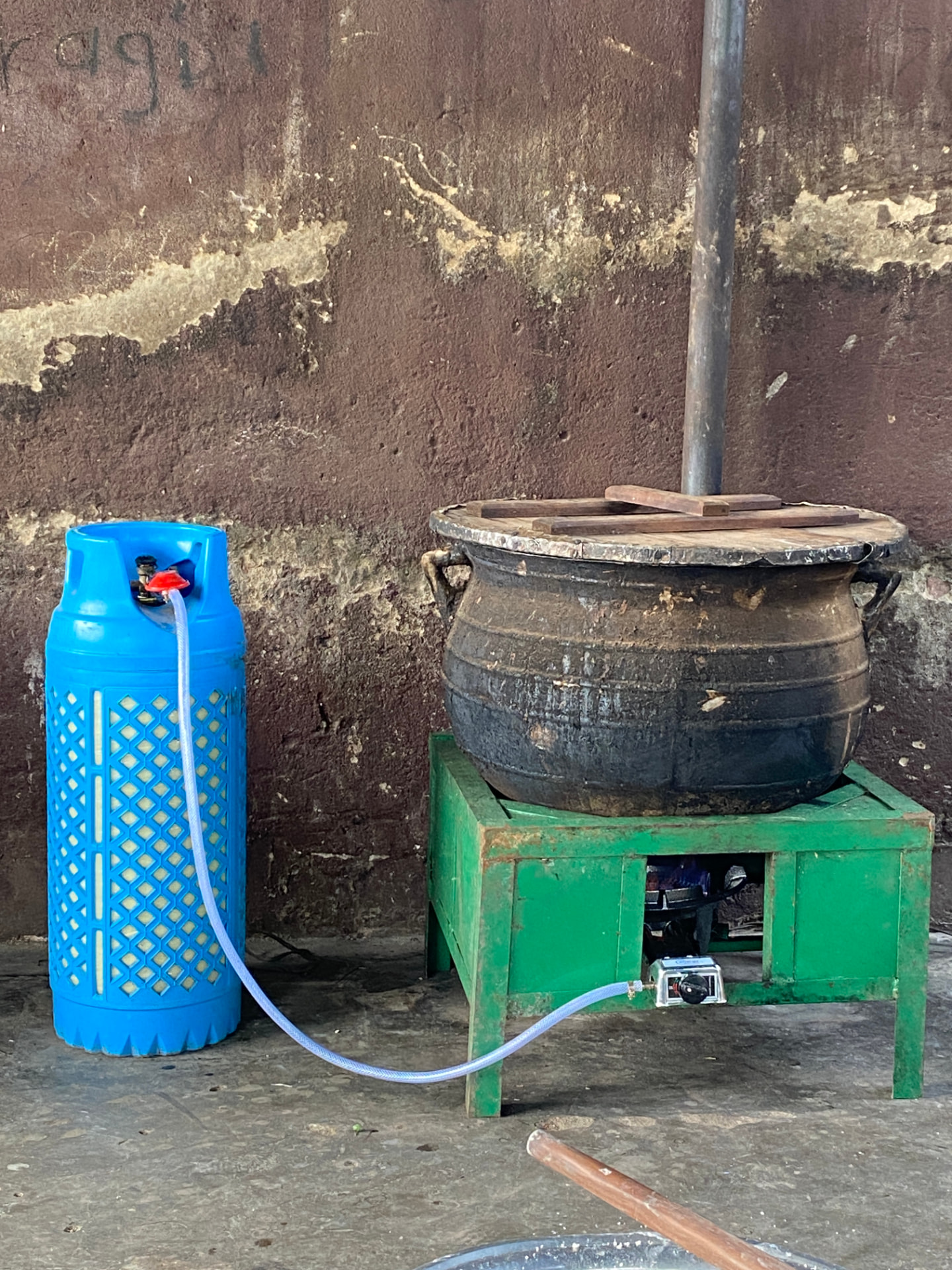 Large cooking pot on a green stove connected by a hose to a blue gas cylinder at the school project